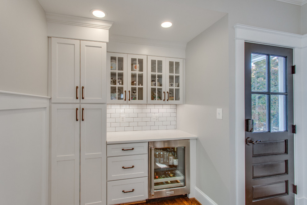 This is an example of a large arts and crafts single-wall eat-in kitchen in DC Metro with an undermount sink, shaker cabinets, white cabinets, quartz benchtops, white splashback, ceramic splashback, stainless steel appliances, medium hardwood floors, with island, brown floor and white benchtop.