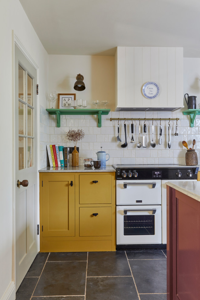 Inredning av ett klassiskt stort grå grått kök, med skåp i shakerstil, gula skåp, marmorbänkskiva, vitt stänkskydd, stänkskydd i keramik, vita vitvaror, kalkstensgolv, en köksö och svart golv