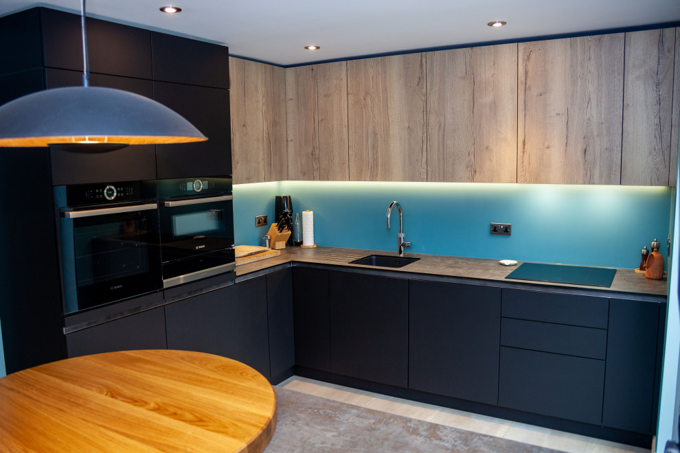 Inspiration for a mid-sized contemporary open plan kitchen in Other with a single-bowl sink, flat-panel cabinets, blue splashback, glass sheet splashback and black appliances.