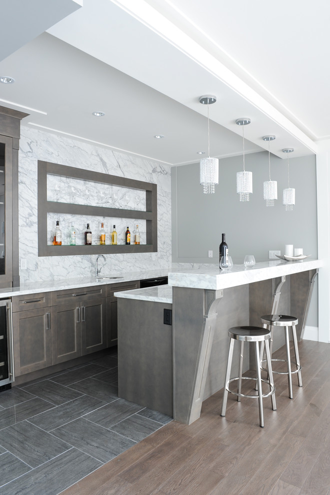 This is an example of a mid-sized transitional u-shaped seated home bar in Vancouver with shaker cabinets, brown cabinets, white splashback, marble splashback, porcelain floors and grey floor.