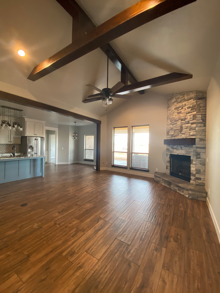 This is an example of a large arts and crafts open concept living room in Oklahoma City with grey walls, porcelain floors, a corner fireplace, a stone fireplace surround and brown floor.