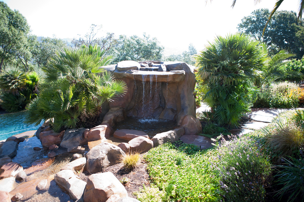 Photo of a large mediterranean backyard custom-shaped natural pool in San Francisco with a water feature and natural stone pavers.