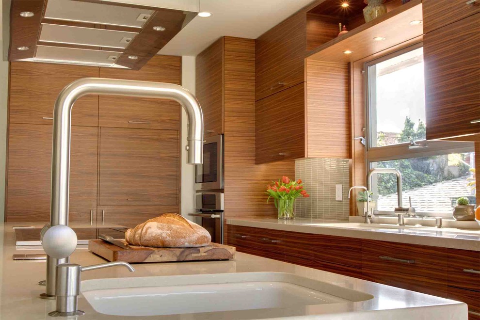 Photo of a large contemporary l-shaped open plan kitchen in Los Angeles with an undermount sink, flat-panel cabinets, medium wood cabinets, quartz benchtops, glass tile splashback, stainless steel appliances, with island and porcelain floors.