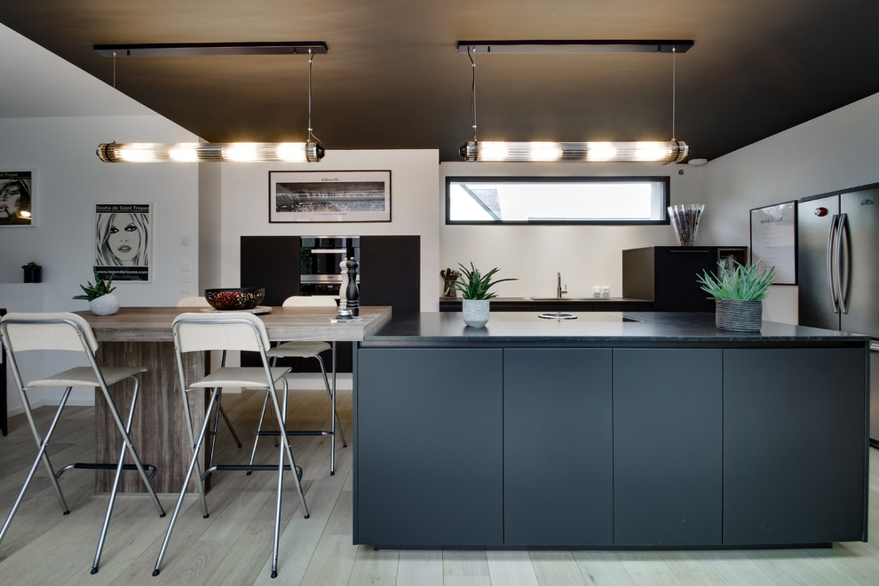Photo of a mid-sized contemporary l-shaped open plan kitchen in Rennes with a single-bowl sink, flat-panel cabinets, black cabinets, granite benchtops, stainless steel appliances, light hardwood floors, multiple islands and black benchtop.