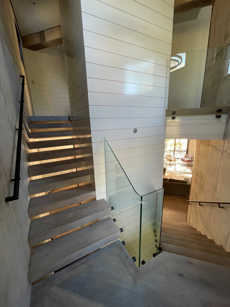 Photo of a contemporary wood floating staircase in Charleston with open risers, glass railing and planked wall panelling.