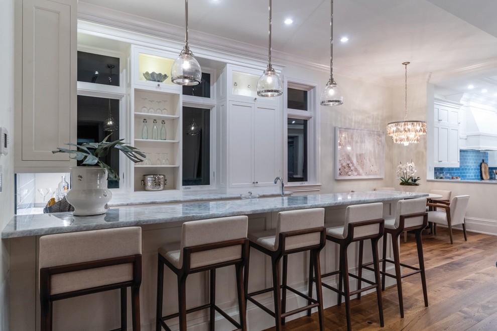 This is an example of an expansive traditional seated home bar in Miami with an undermount sink, recessed-panel cabinets, white cabinets, onyx benchtops, medium hardwood floors and blue benchtop.