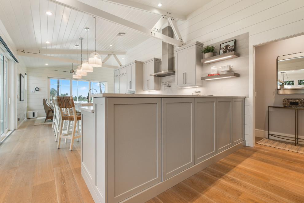 Design ideas for a mid-sized beach style l-shaped open plan kitchen in Other with an undermount sink, grey cabinets, quartz benchtops, stainless steel appliances, light hardwood floors, with island, grey floor and white benchtop.