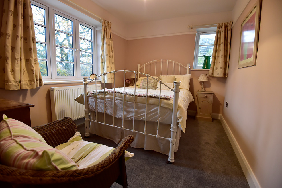 This is an example of a small midcentury guest bedroom in Hertfordshire with pink walls, carpet and grey floor.