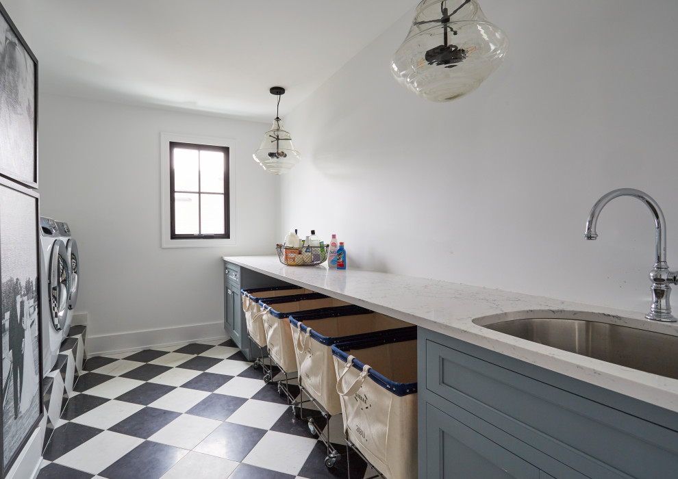 Photo of a large farmhouse galley separated utility room in Chicago with a submerged sink, beaded cabinets, blue cabinets, composite countertops, white walls, concrete flooring, a side by side washer and dryer, black floors and white worktops.