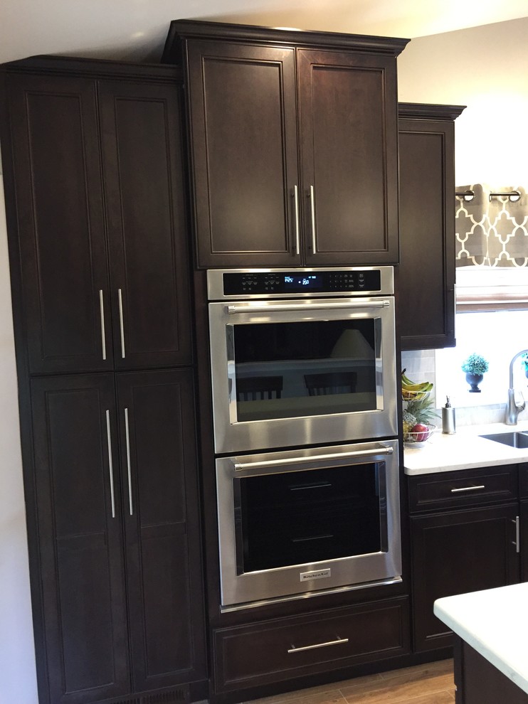 Large contemporary single-wall eat-in kitchen in Philadelphia with an undermount sink, recessed-panel cabinets, dark wood cabinets, quartz benchtops, grey splashback, subway tile splashback, stainless steel appliances, porcelain floors and multiple islands.