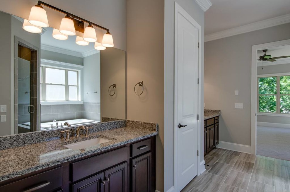 Mid-sized transitional 3/4 gray tile and porcelain tile porcelain tile and gray floor corner shower photo with recessed-panel cabinets, black cabinets, beige walls, an undermount sink, granite countertops and a hinged shower door