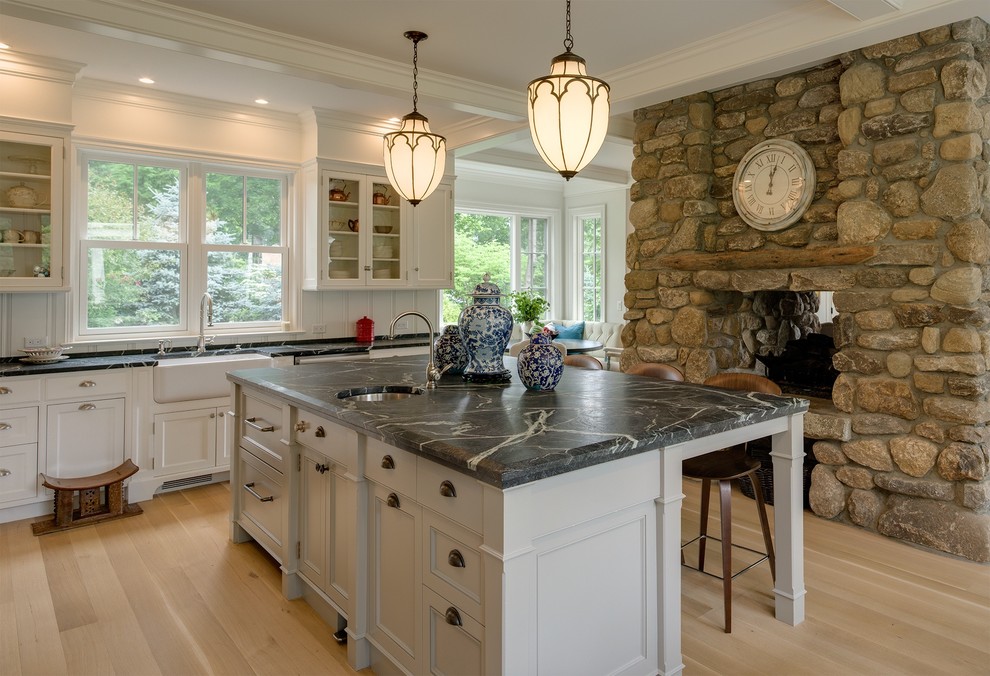 Inspiration for a traditional u-shaped eat-in kitchen in New York with a farmhouse sink, recessed-panel cabinets, white cabinets, soapstone benchtops, white splashback, stainless steel appliances, light hardwood floors and with island.