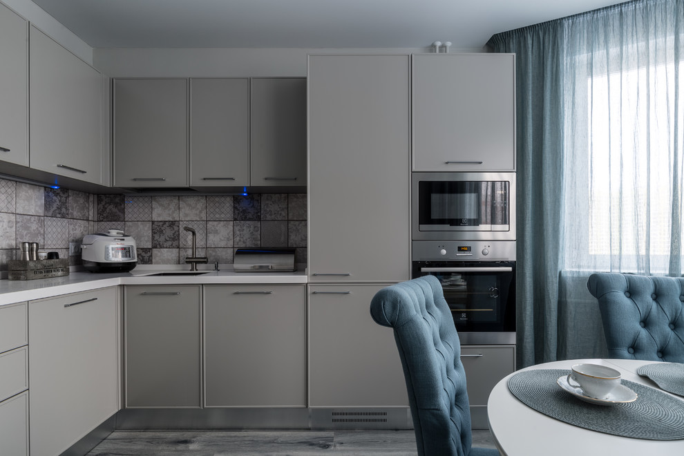 Photo of a contemporary l-shaped eat-in kitchen in Moscow with an undermount sink, beaded inset cabinets, grey cabinets, grey splashback, grey floor, no island and white benchtop.
