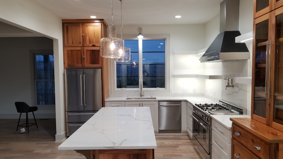 Mid-sized transitional l-shaped light wood floor and brown floor kitchen photo with an undermount sink, recessed-panel cabinets, white cabinets, marble countertops, white backsplash, marble backsplash, stainless steel appliances, an island and white countertops