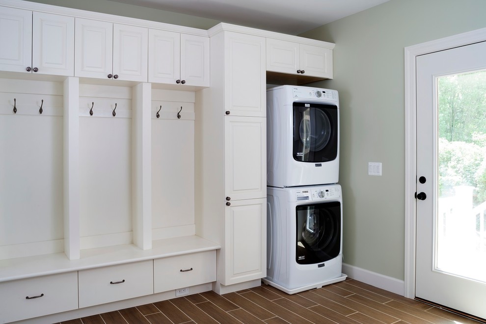 This is an example of a mid-sized transitional utility room in DC Metro with raised-panel cabinets, white cabinets, vinyl floors, a stacked washer and dryer, brown floor and grey walls.
