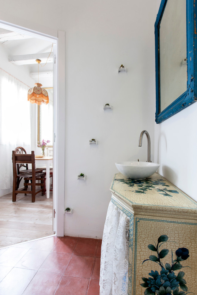 This is an example of a mid-sized eclectic powder room in Madrid with open cabinets, white walls, terra-cotta floors and a vessel sink.