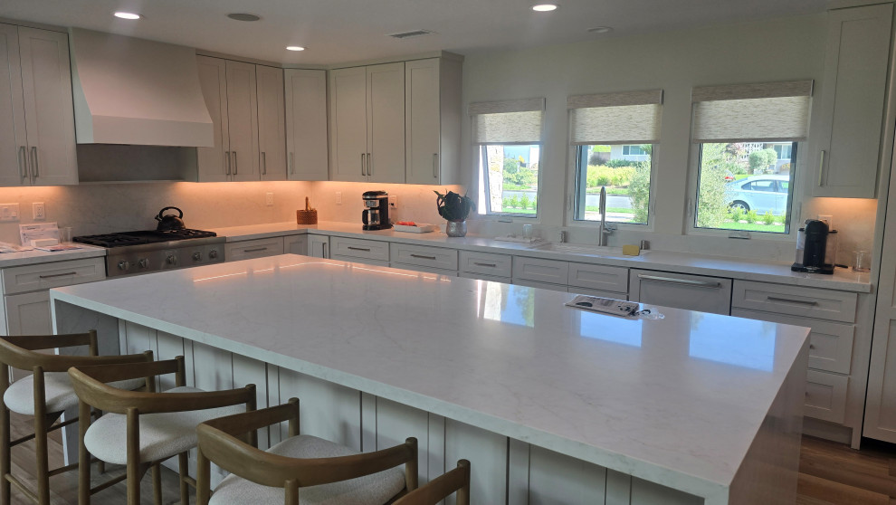 Open concept kitchen - mid-sized l-shaped vinyl floor and gray floor open concept kitchen idea in Orange County with an undermount sink, shaker cabinets, white cabinets, quartz countertops, stainless steel appliances, an island, white countertops, white backsplash and quartz backsplash