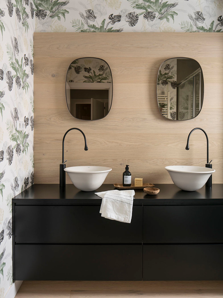 This is an example of a mid-sized beach style powder room in Barcelona with black cabinets, multi-coloured walls, light hardwood floors, a vessel sink, laminate benchtops, brown floor, black benchtops and flat-panel cabinets.