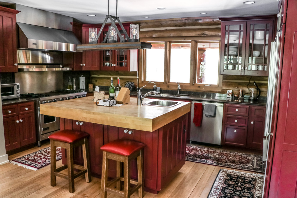Large mountain style u-shaped light wood floor and brown floor kitchen photo with an undermount sink, flat-panel cabinets, red cabinets, wood countertops, brown backsplash, wood backsplash, stainless steel appliances, an island and brown countertops