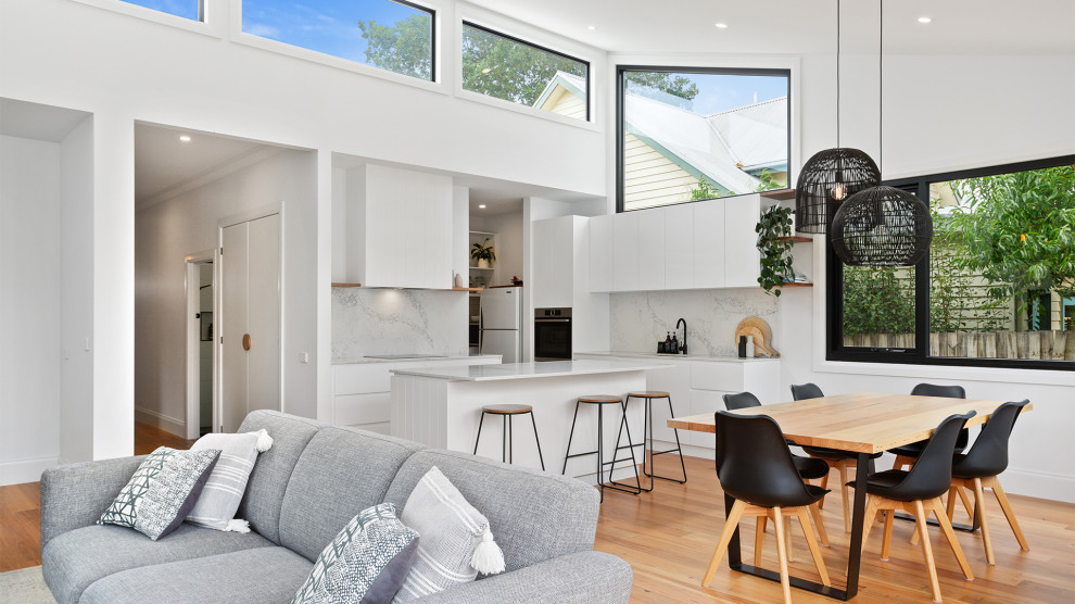 This is an example of a small contemporary l-shaped open plan kitchen in Geelong with flat-panel cabinets, white cabinets, white splashback, medium hardwood floors, with island, brown floor, white benchtop and vaulted.