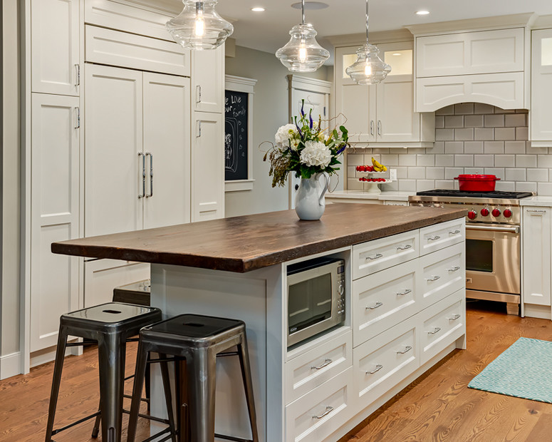 Mid-sized transitional l-shaped light wood floor and beige floor enclosed kitchen photo in Calgary with a farmhouse sink, recessed-panel cabinets, white cabinets, quartz countertops, white backsplash, porcelain backsplash, stainless steel appliances and an island