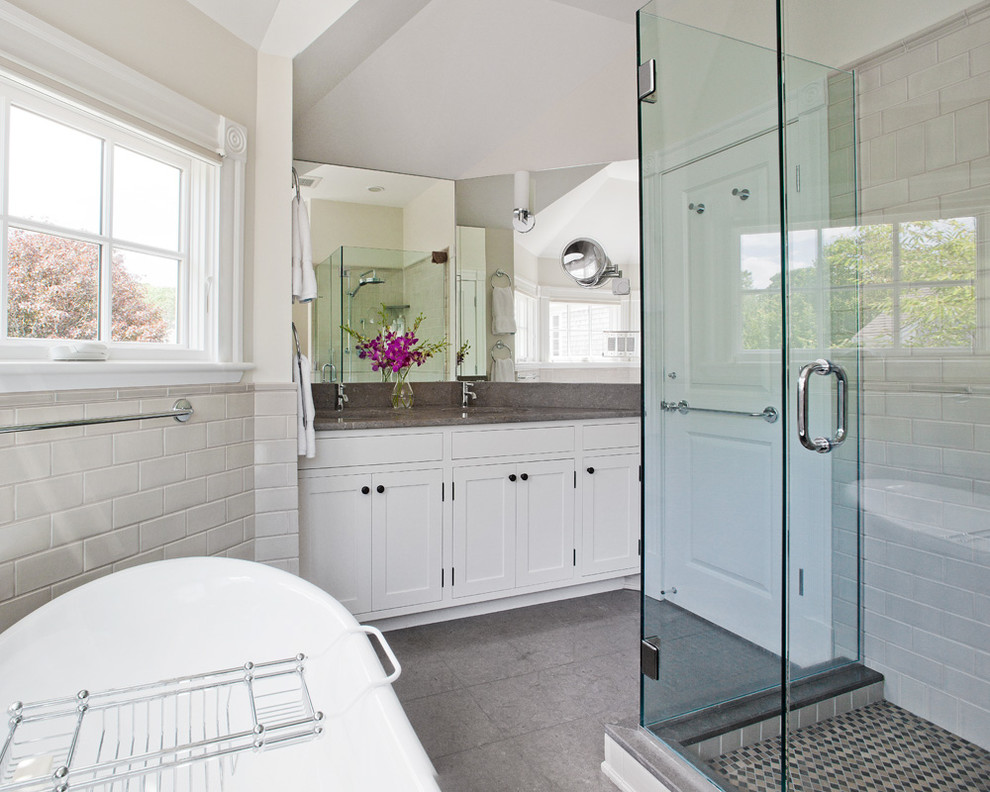 This is an example of a beach style bathroom in New York with shaker cabinets, white cabinets, a freestanding tub, a corner shower, gray tile and subway tile.