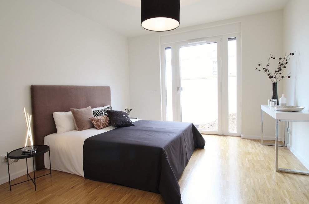 This is an example of a contemporary guest bedroom in Bremen with white walls, medium hardwood flooring and brown floors.