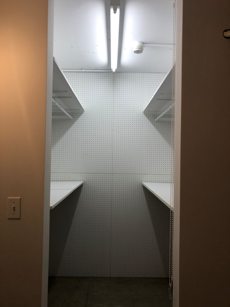 Immagine di una piccola cabina armadio unisex moderna con pavimento in cemento e travi a vista