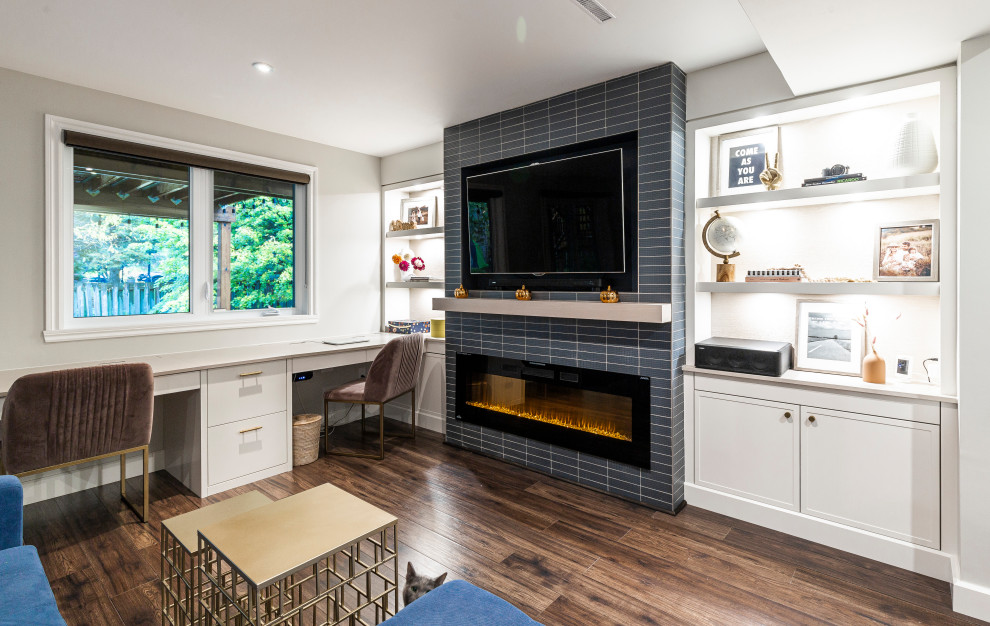 Cette image montre un bureau atelier traditionnel de taille moyenne avec un mur gris, sol en stratifié, une cheminée standard, un manteau de cheminée en carrelage, un bureau intégré et un sol marron.