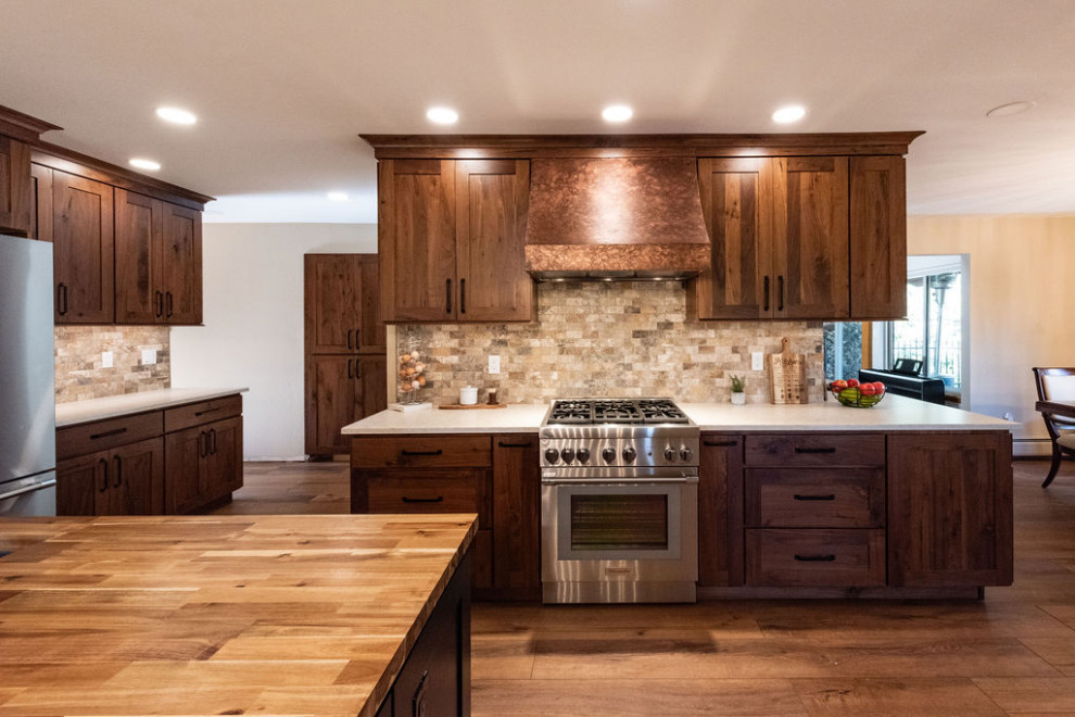Large industrial eat-in kitchen in Denver with a farmhouse sink, recessed-panel cabinets, dark wood cabinets, quartzite benchtops, multi-coloured splashback, travertine splashback, stainless steel appliances, dark hardwood floors, with island, brown floor and white benchtop.