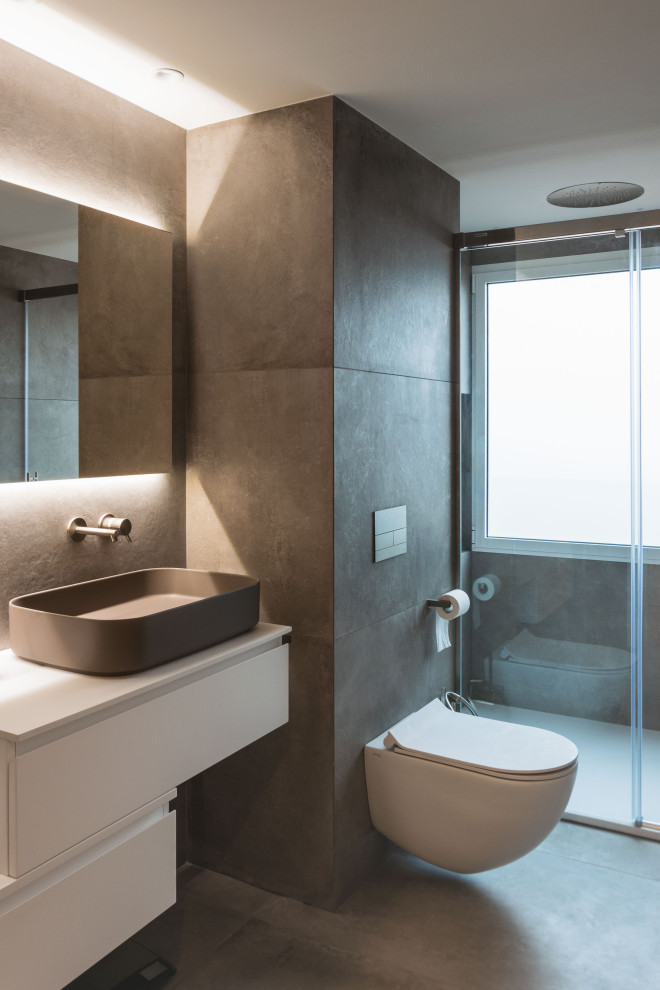 This is an example of a mid-sized modern master wet room bathroom in Valencia with furniture-like cabinets, grey cabinets, a one-piece toilet, gray tile, ceramic tile, grey walls, ceramic floors, a vessel sink, grey floor, a sliding shower screen, an enclosed toilet, a single vanity and a built-in vanity.