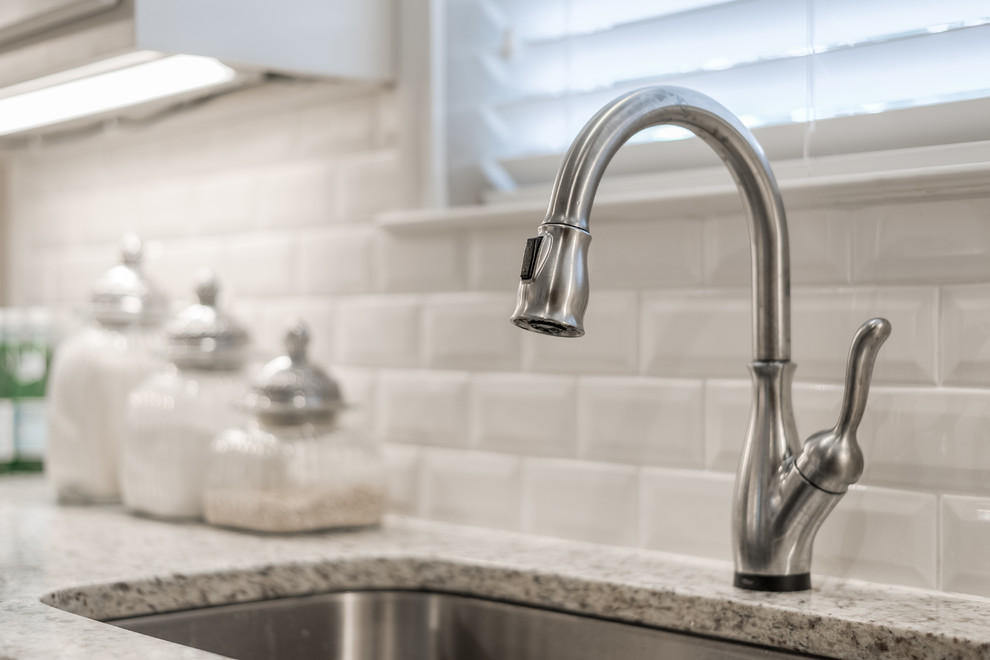 Inspiration for a mid-sized transitional galley medium tone wood floor enclosed kitchen remodel in Dallas with an undermount sink, raised-panel cabinets, white cabinets, granite countertops, white backsplash, subway tile backsplash, stainless steel appliances and a peninsula