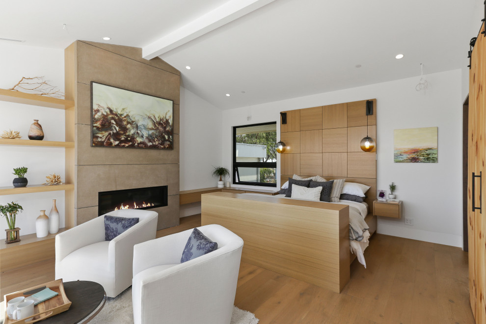 Geräumiges Modernes Hauptschlafzimmer mit weißer Wandfarbe, braunem Holzboden, Gaskamin, gewölbter Decke, Kaminumrandung aus Stein und beigem Boden in Orange County