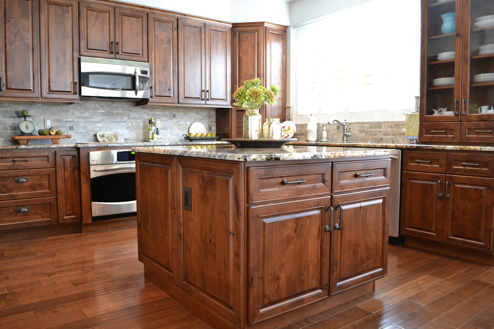 Mid-sized transitional u-shaped medium tone wood floor eat-in kitchen photo in Phoenix with an undermount sink, raised-panel cabinets, distressed cabinets, granite countertops, gray backsplash, stone tile backsplash, stainless steel appliances and an island