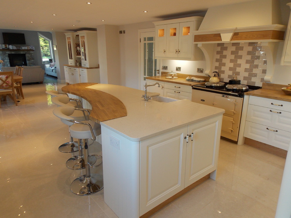 Mid-sized traditional open plan kitchen in Dublin with a farmhouse sink, raised-panel cabinets, white cabinets, wood benchtops, ceramic splashback, porcelain floors and with island.