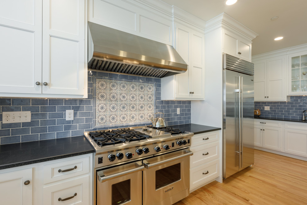 Inspiration for a large traditional kitchen in Other with an undermount sink, shaker cabinets, white cabinets, granite benchtops, blue splashback, glass tile splashback, stainless steel appliances, light hardwood floors, with island and black benchtop.