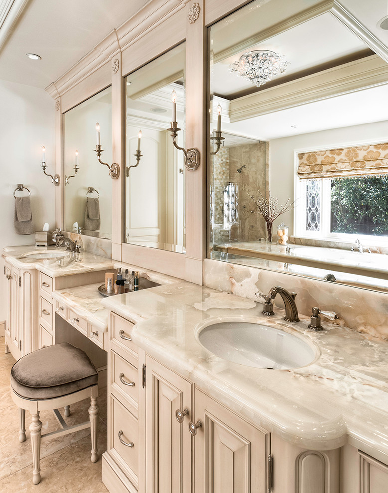 This is an example of a mid-sized traditional master bathroom in San Francisco with an undermount sink, furniture-like cabinets, onyx benchtops, an undermount tub, yellow tile, stone tile, beige walls and limestone floors.