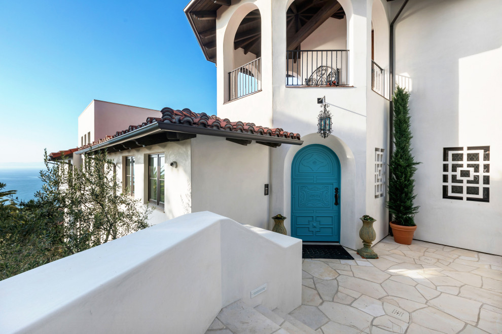 ロサンゼルスにある広い地中海スタイルのおしゃれな玄関ドア (青い壁、ライムストーンの床、青いドア、ベージュの床) の写真