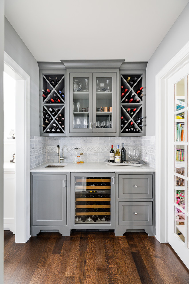 Mid-sized transitional single-wall wet bar in Chicago with an undermount sink, beaded inset cabinets, grey cabinets, quartz benchtops, grey splashback, marble splashback, medium hardwood floors and brown floor.