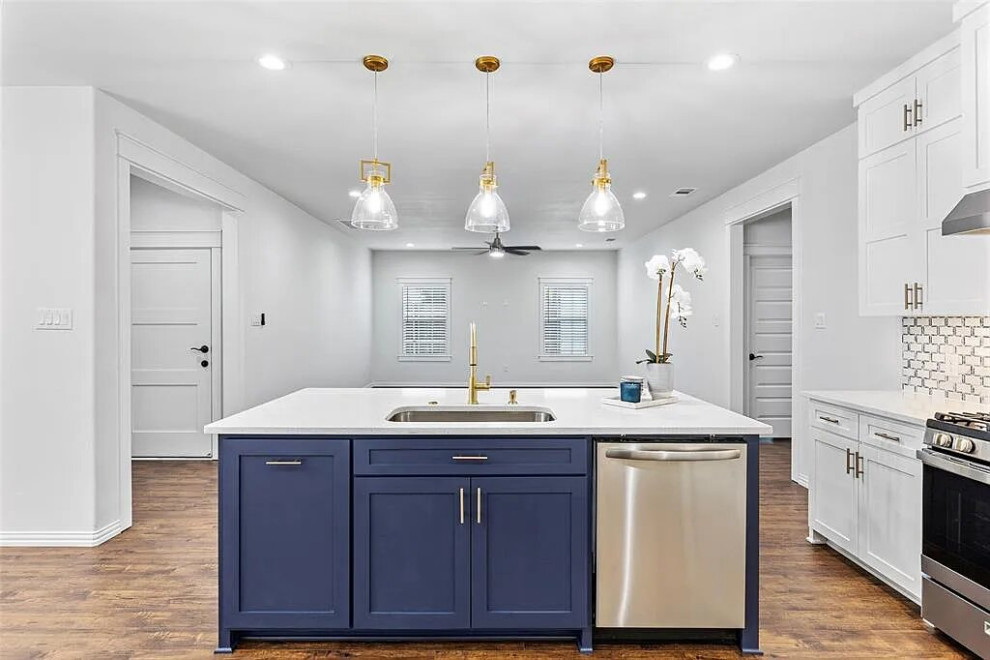 This is an example of a large transitional l-shaped kitchen pantry in Houston with a farmhouse sink, shaker cabinets, white cabinets, quartzite benchtops, white splashback, porcelain splashback, stainless steel appliances, medium hardwood floors, with island, brown floor, white benchtop and coffered.