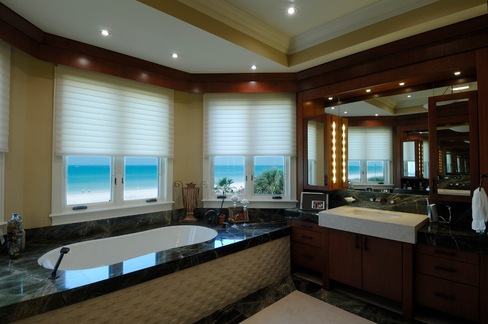 Design ideas for a large eclectic master bathroom in Tampa with an undermount sink, flat-panel cabinets, medium wood cabinets, granite benchtops, an undermount tub, beige tile, stone tile, yellow walls and marble floors.