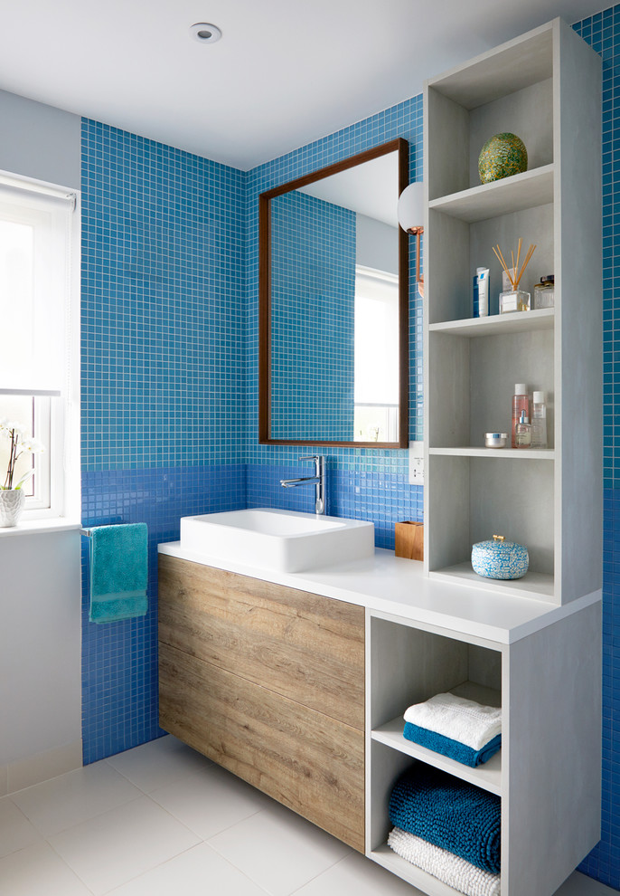 Photo of a transitional kids bathroom in London with blue tile, white floor, flat-panel cabinets, medium wood cabinets, mosaic tile, blue walls, a vessel sink and white benchtops.