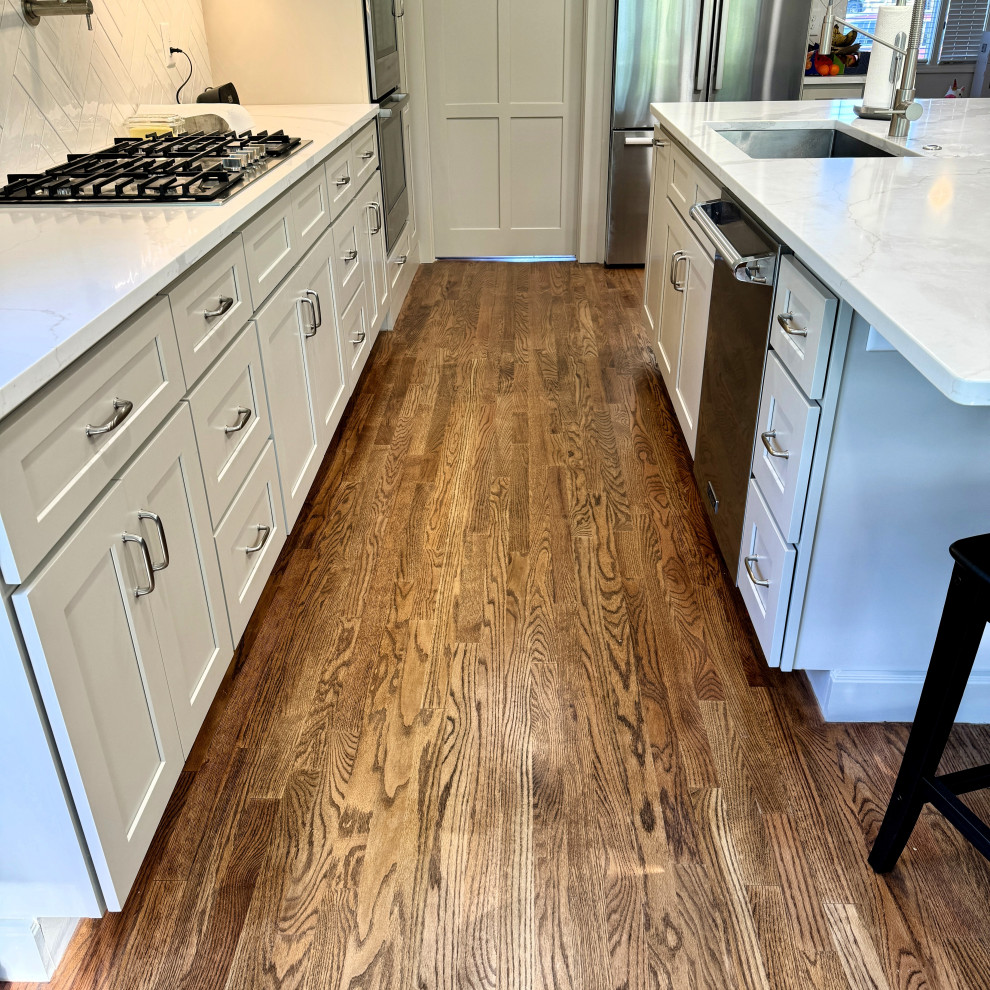 Open concept kitchen - mid-sized transitional u-shaped medium tone wood floor and brown floor open concept kitchen idea in Atlanta with an undermount sink, shaker cabinets, granite countertops, white backsplash, stainless steel appliances, an island, white countertops and beige cabinets