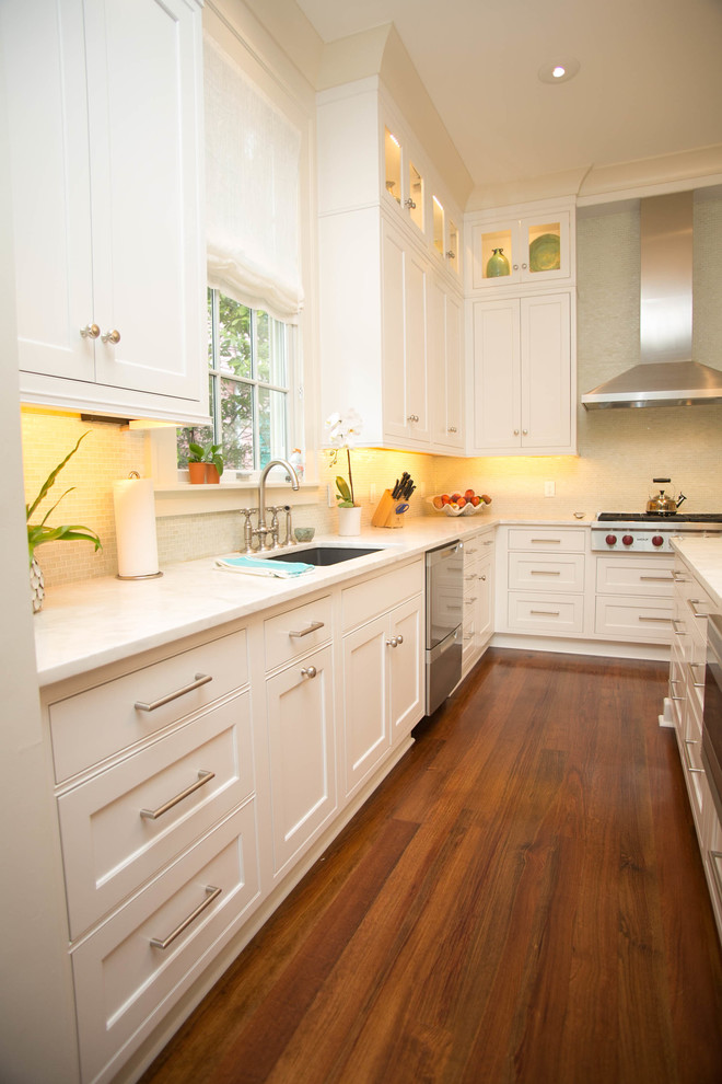 Design ideas for a mid-sized traditional l-shaped eat-in kitchen in New Orleans with an undermount sink, recessed-panel cabinets, white cabinets, marble benchtops, white splashback, mosaic tile splashback, stainless steel appliances, light hardwood floors and with island.
