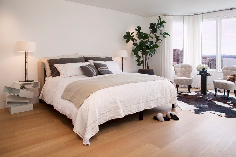 This is an example of a contemporary master bedroom in San Francisco with white walls and light hardwood floors.