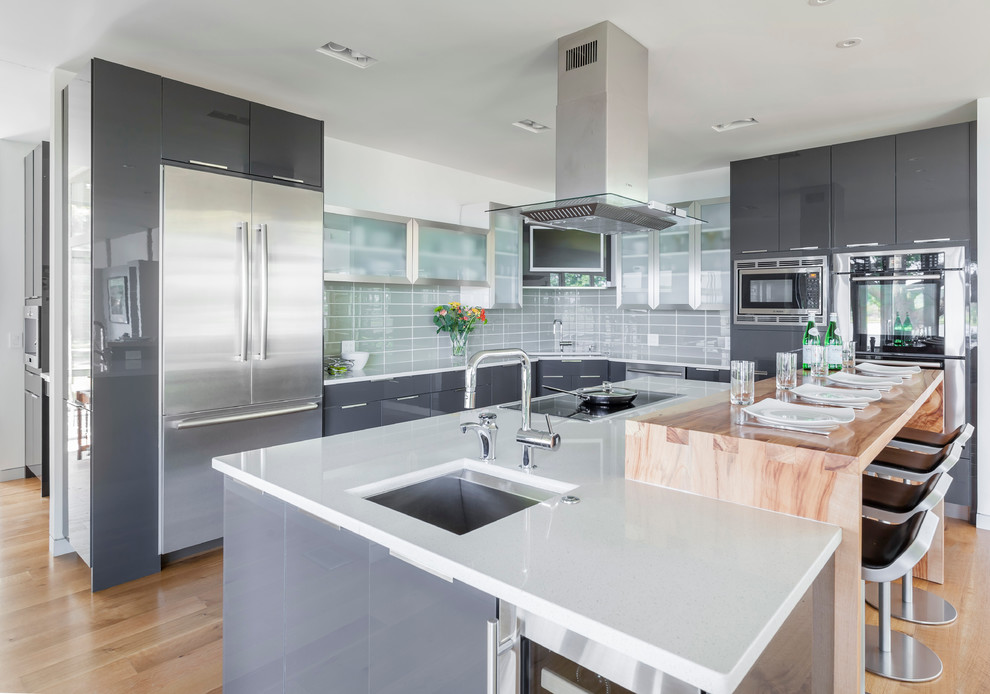 Photo of a mid-sized contemporary l-shaped open plan kitchen in Baltimore with an undermount sink, flat-panel cabinets, grey cabinets, grey splashback, glass tile splashback, stainless steel appliances, light hardwood floors and with island.