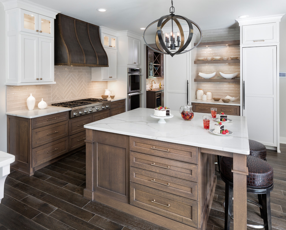Design ideas for a large transitional u-shaped eat-in kitchen in Minneapolis with a farmhouse sink, recessed-panel cabinets, brown cabinets, quartzite benchtops, grey splashback, glass tile splashback, panelled appliances, dark hardwood floors, with island and brown floor.