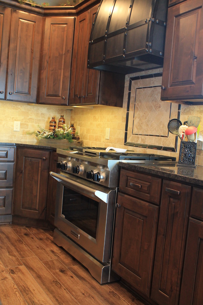 Example of a mid-sized mountain style u-shaped medium tone wood floor kitchen design with raised-panel cabinets, dark wood cabinets, granite countertops, beige backsplash, ceramic backsplash, black appliances and an island