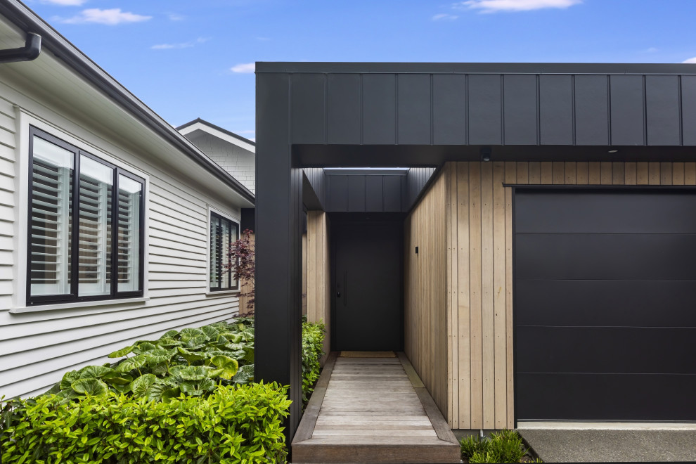 Photo of a mid-sized contemporary front door in Christchurch with beige walls, medium hardwood floors, a single front door, a black front door, beige floor and planked wall panelling.