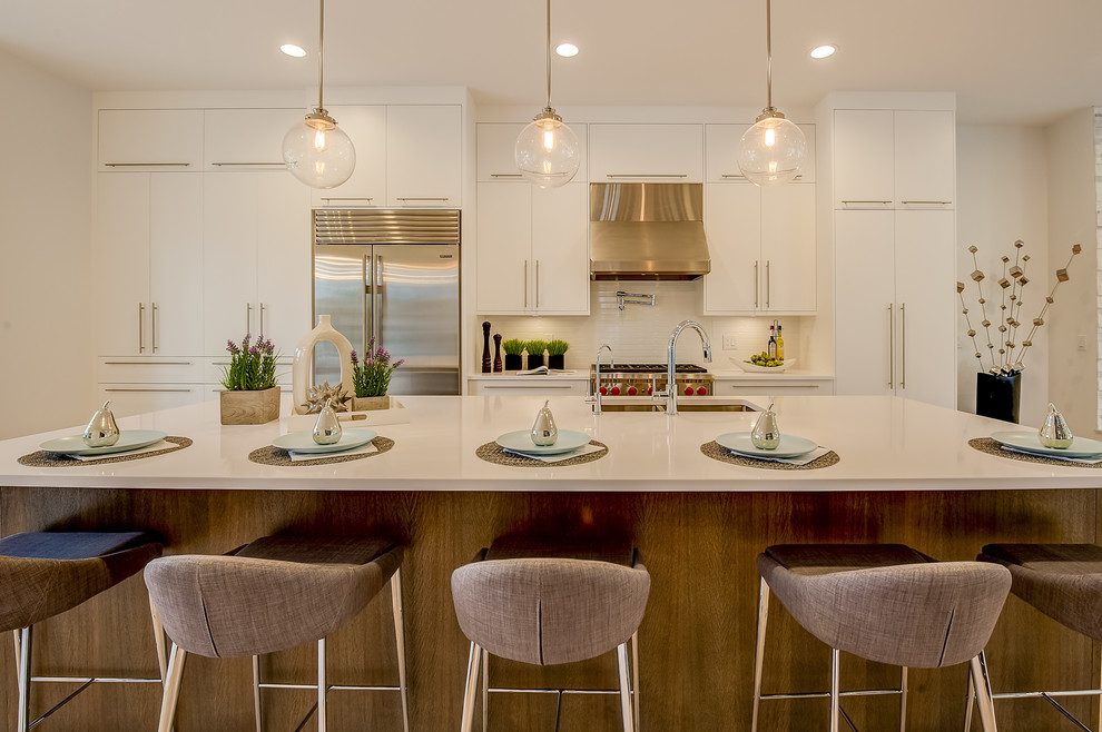 Transitional galley kitchen photo in Calgary with an undermount sink, flat-panel cabinets, white cabinets, white backsplash, subway tile backsplash, stainless steel appliances and an island